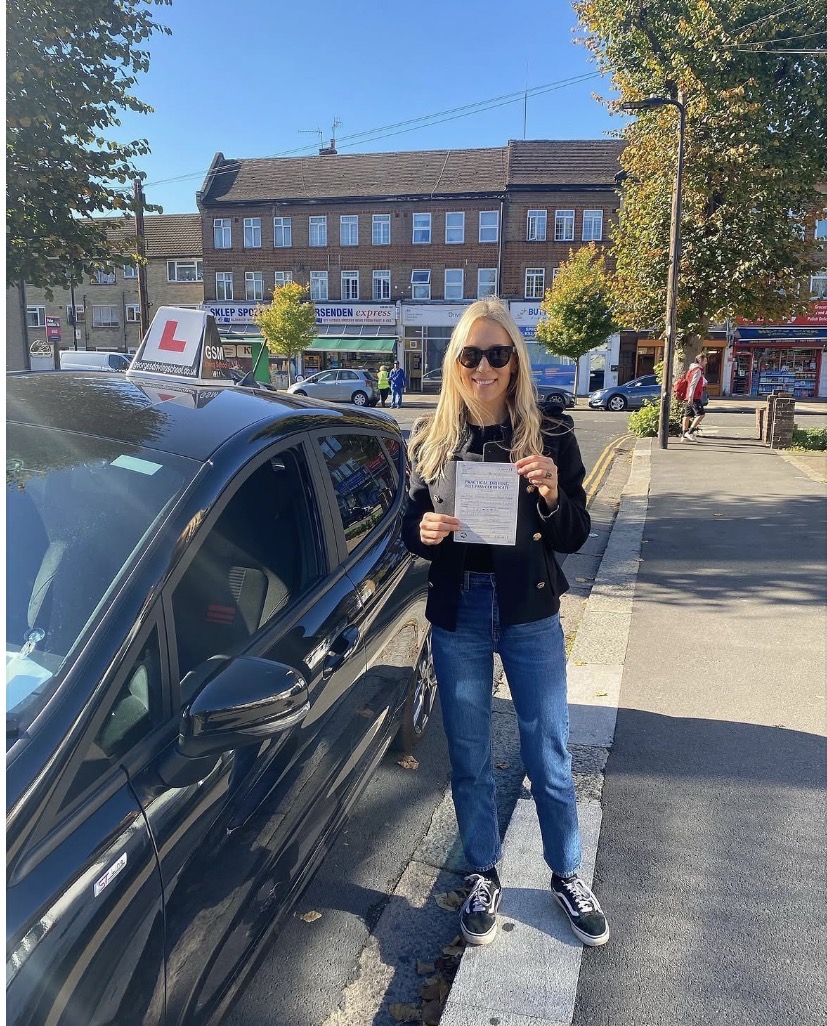 A happy GSM student holding their practical driving test pass certificate next to the GSM car
